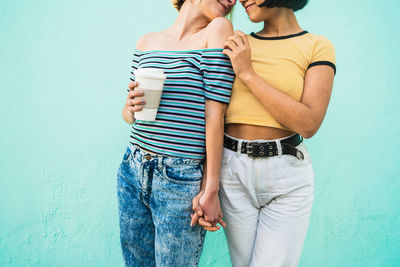 Midsection of friends holding hands standing against wall