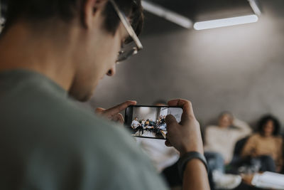 Young businessman photographing colleagues through smart phone at creative office