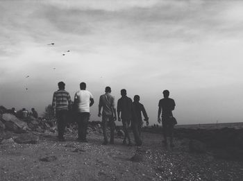 Rear view of men walking on field against sky