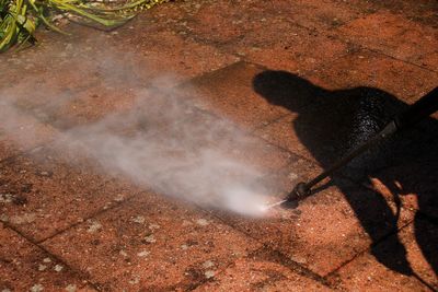 High angle view of person spraying water on footpath during sunny day