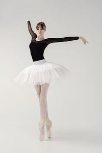 A ballerina in a bodysuit and tutu poses in motion showing ballet elements while standing on pointes