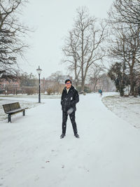 Portrait of man standing on snowy road against bare trees