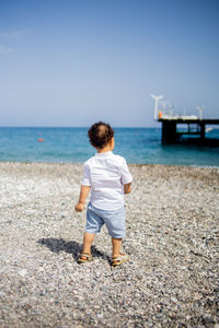 Happy toddler boy in white shirt and blue shorts on the beach