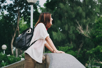 Side view of happy woman standing on bridge against trees