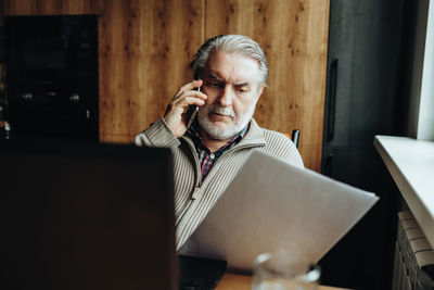 An elderly man works at a laptop, learning from home, home bookkeeping