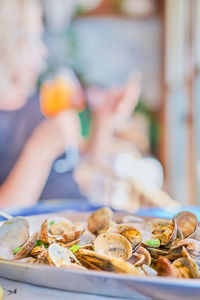 Blurred background, dish of boiled vongole clams,  silhouette of woman with  glass of wine