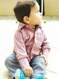 Full length of cute boy looking away while sitting on floor