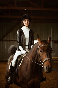 A jockey girl in full dress sits on a horse. depicted body fragment