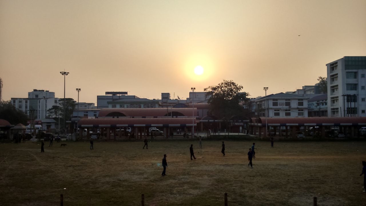 building exterior, architecture, built structure, sunset, city, sky, silhouette, sun, building, clear sky, street light, orange color, outdoors, sunlight, bird, residential building, incidental people, residential structure, city life, dusk