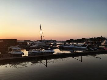 Sailboats moored at harbor against clear sky during sunset