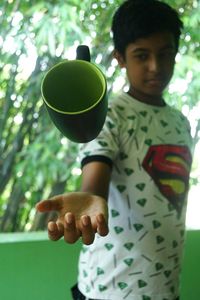 Boy catching cup while standing against trees