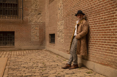 Portrait of adult man in hat and coat against wall on street