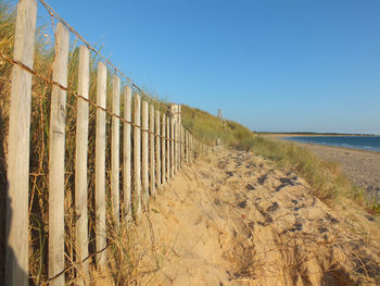 Wooden fence on sand at beach against clear sky