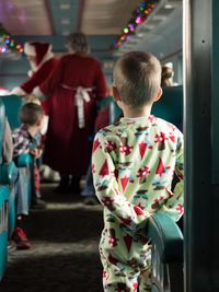 Rear view of boy looking at people dressed as santa claus in train