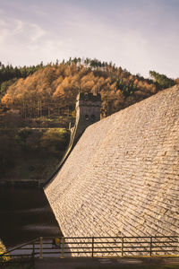 Derwent reservoir by trees on mountain against sky