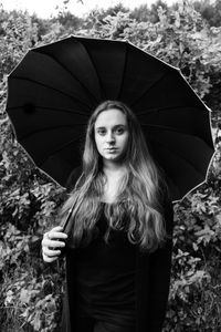 Portrait of young woman standing against trees