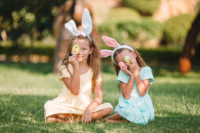 Sisters holding easter eggs while sitting at lawn