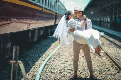 Groom carrying bride and looking at each other while standing on rail road track