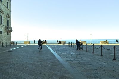 People walking on footpath by sea against clear sky