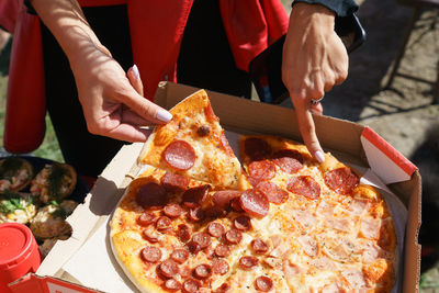 Person is holding slice pepperoni pizza is cut in  half having pepperoni and other half having ham