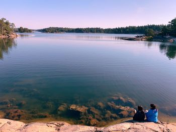 Rear view of men sitting on lake against sky