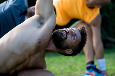 Close-up of shirtless man with friends exercising in lawn
