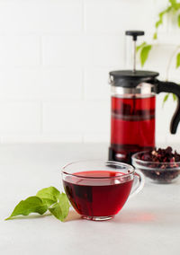 Herbal tea made from hibiscus petals in a transparent cup on a light background, teapot 