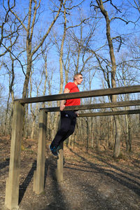 Side view of young man hanging from monkey bars at forest
