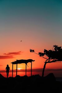 Silhouette woman standing at beach against orange sky