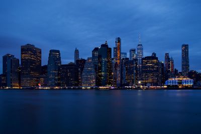 Illuminated buildings by sea against sky at dusk