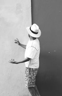 Side view of man wearing hat while standing by wall