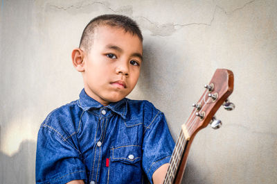 Portrait of boy with musical instrument by wall