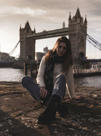 Woman sitting on bridge over river in city