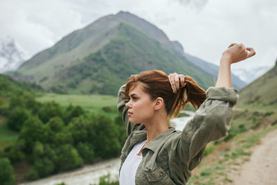 Side view of young woman standing against mountain