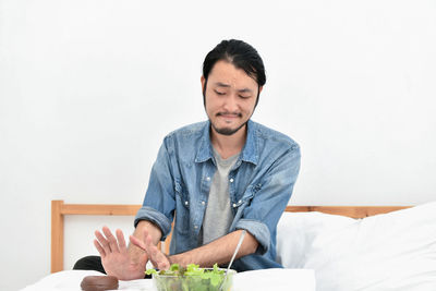 Young man refusing food while sitting against wall