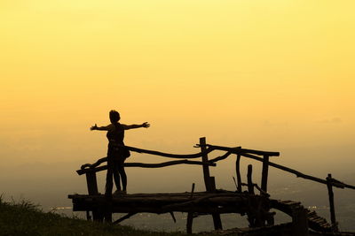 Silhouette woman with arms outstretched standing at observation point at sunset