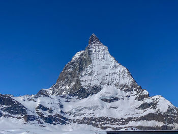 Low angle view of snowcapped mountains against clear blue sky
