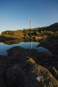 Lighthouse by sea against clear sky