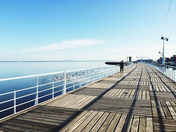 Rear view of man walking on pier by frozen lake against sky