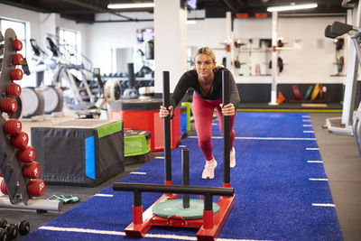 A fit female pushes a weight sled on turf at the gym.