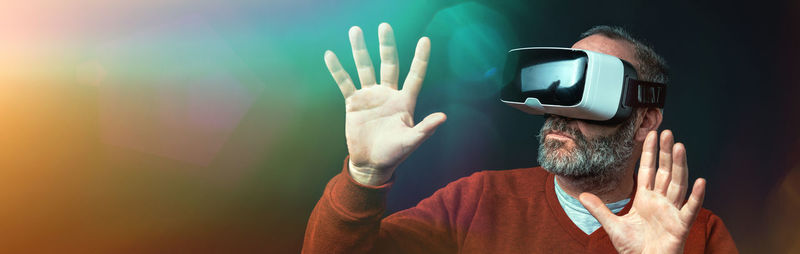 Panoramic view of senior man using virtual reality headset against colored background