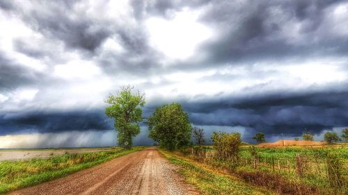 Road passing through field against cloudy sky