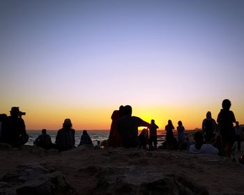 Silhouette people on beach against clear sky during sunset