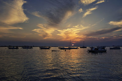 Sailboats moored on sea against sky during sunset