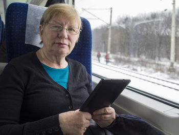 Portrait of senior woman with digital tablet sitting in train