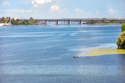 The water surface of the wide dnipro river in the foreground, a lone fisherman on an inflatable boat