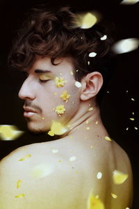 Shirtless young man with petals against black background