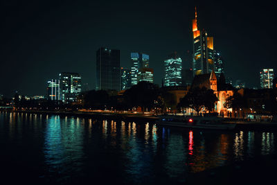 Illuminated buildings by river against sky at night