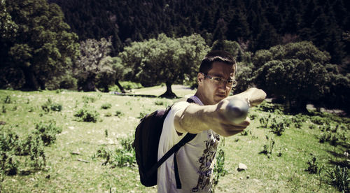 Portrait of male hiker pointing stick while standing on grassy field