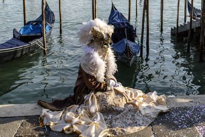 High angle view of person wearing venetian mask while sitting at harbor